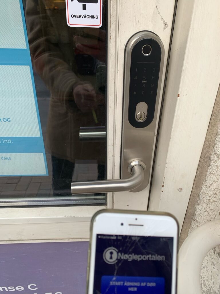 Elektronisk Move-lås på en indgangsdør med en mobiltelefon foran døren.